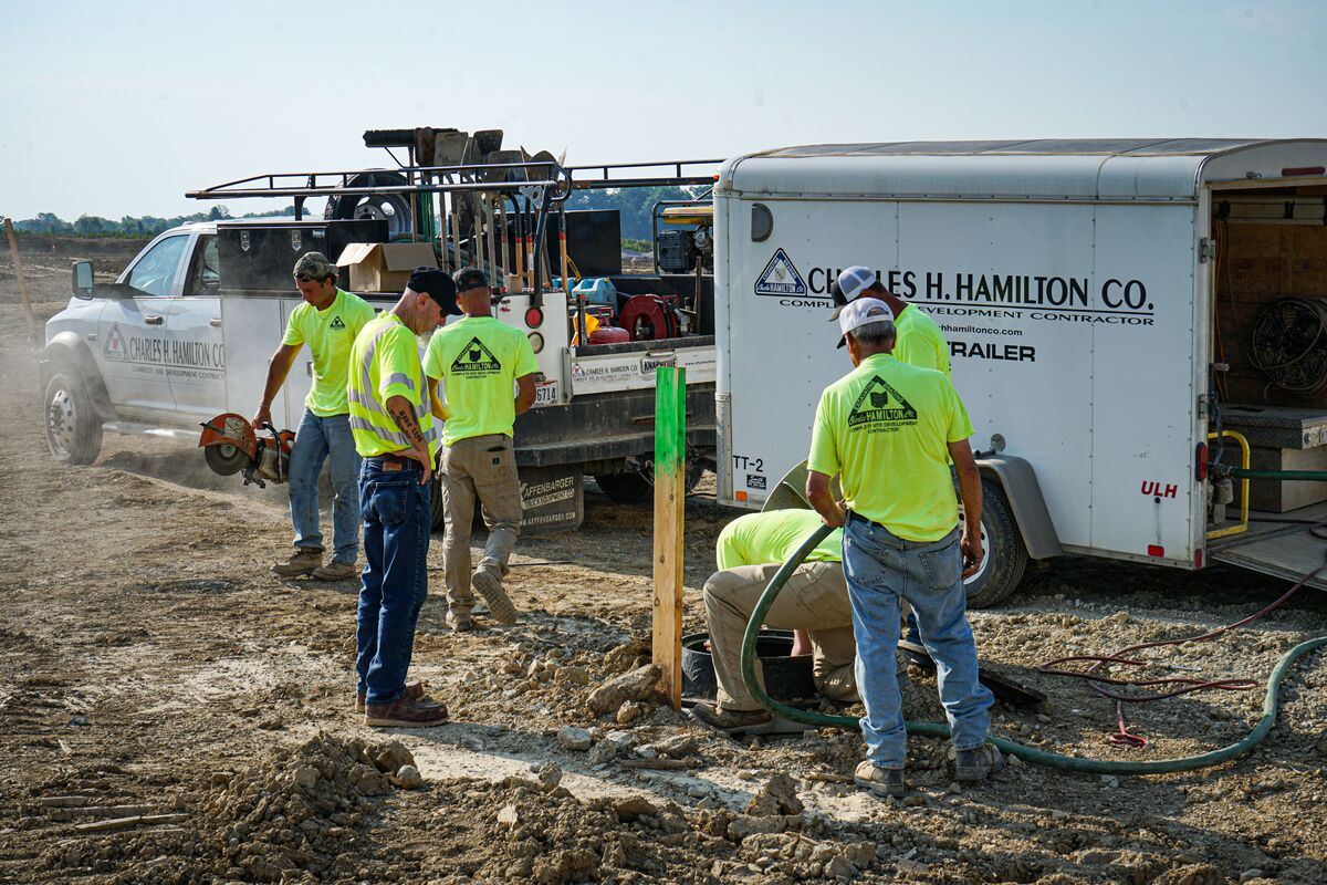 Construction crew installing a utility access structure beside a service trailer at an active job site.